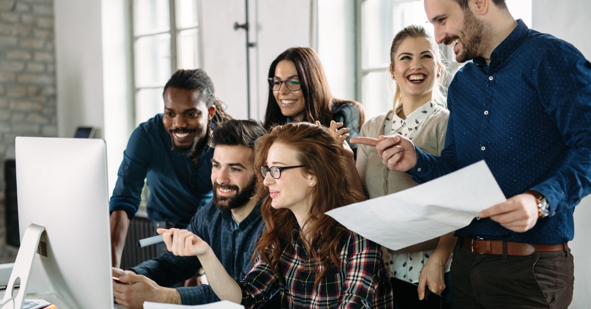 Six coworkers looking at a computer screen and smiling.