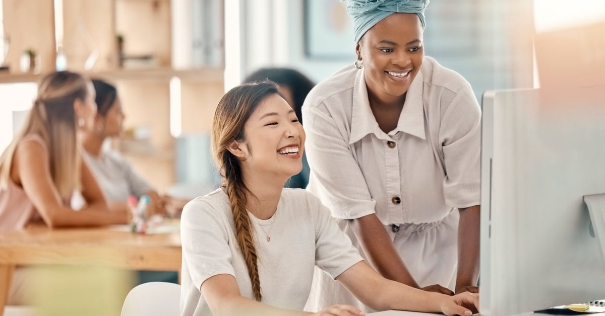Two coworkers smiling and looking at a computer screen.